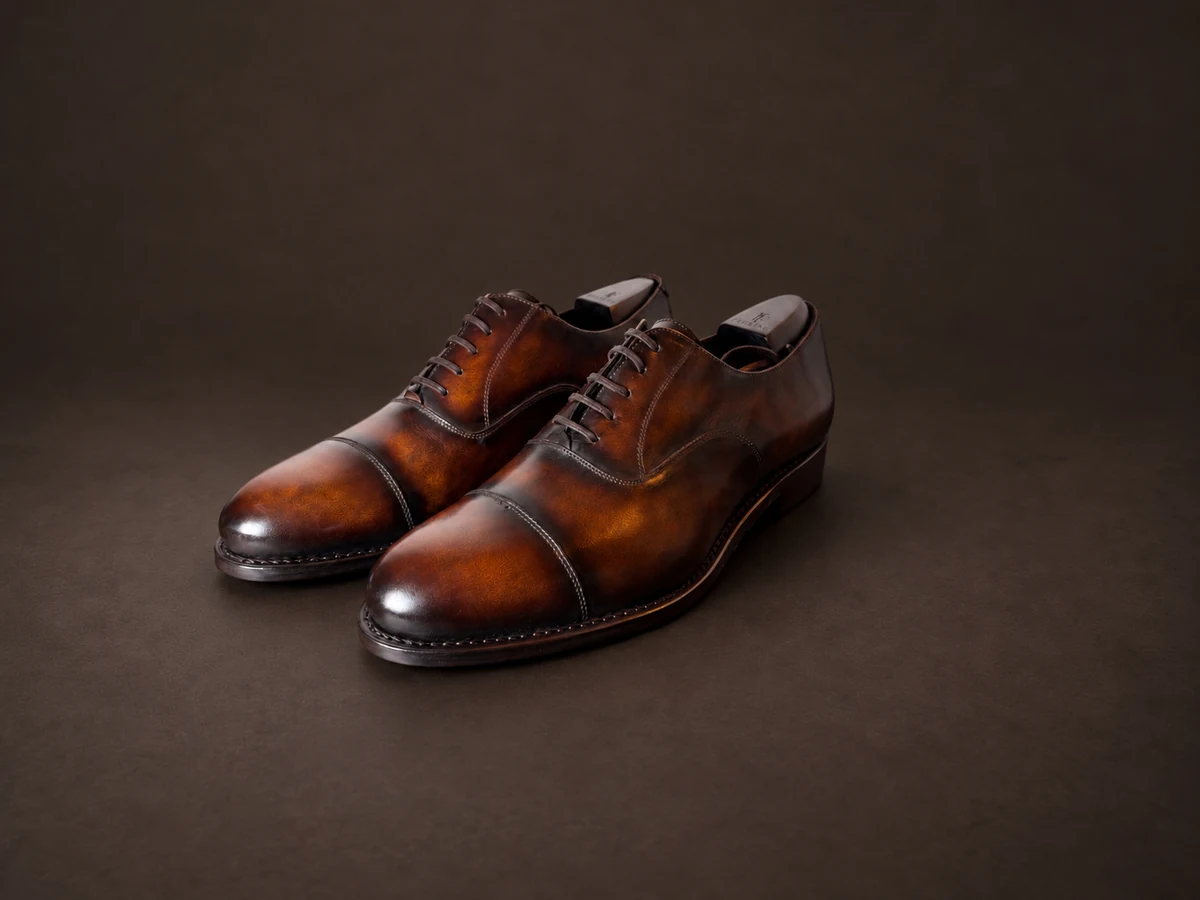FEURING Oxford-Paar mit brauner Tobacco-Patina vor dunklem Hintergrund